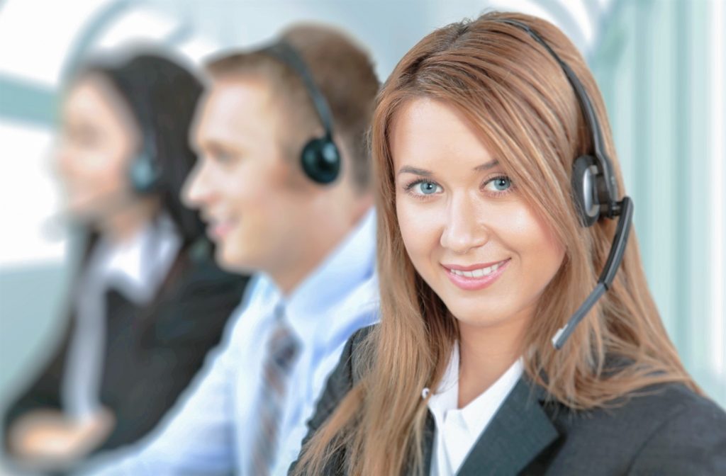 Mujer sonriente con audífonos y micrófonos de call center trabajando con un hombre y una mujer en la oficina