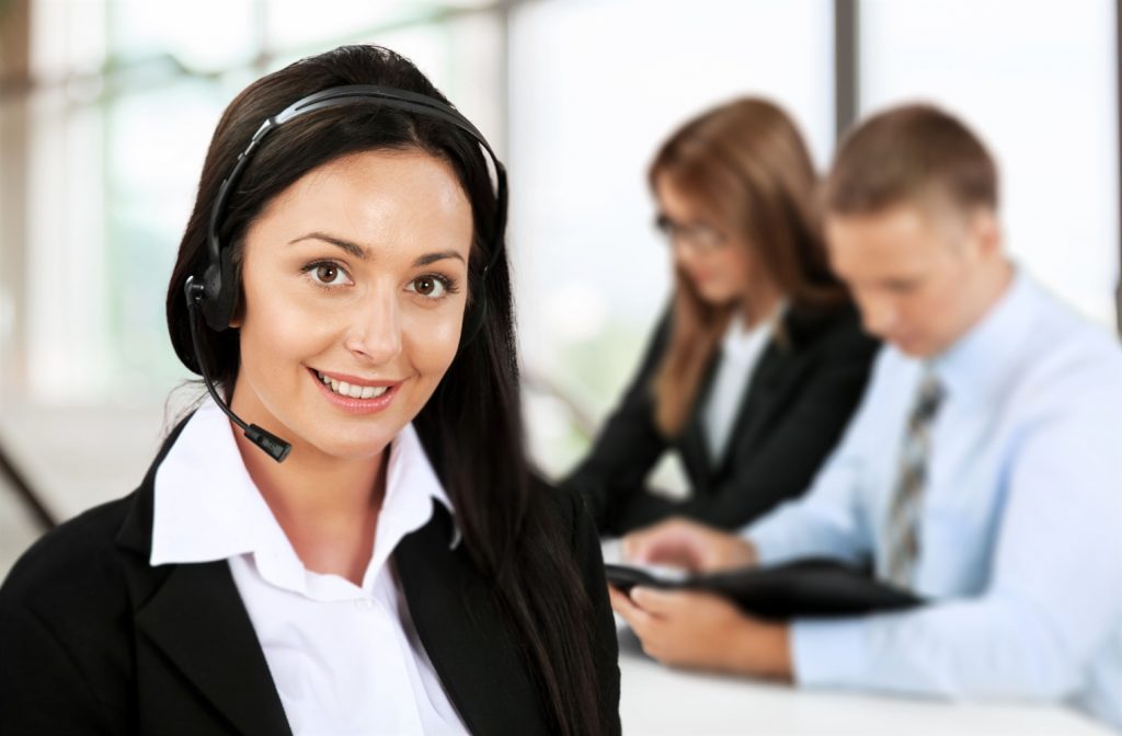Operadora de customer success con audífonos y micrófono de call center con dos clientes detrás de ella